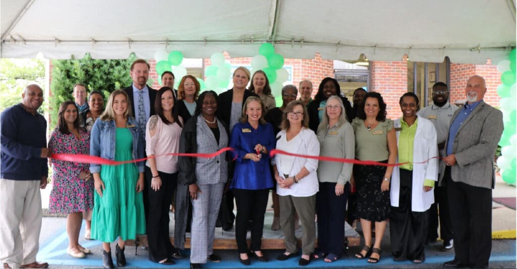 Group photo of the happy stff members of Pee Dee Hearing Center smiling cutting a ribbon in celebration